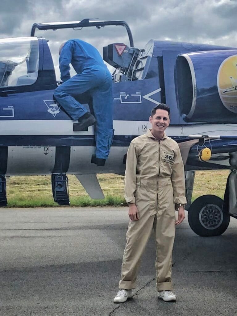 Scoot wearing a professional flight suit in front of the Baltic Bees jet fighter in Latvia.